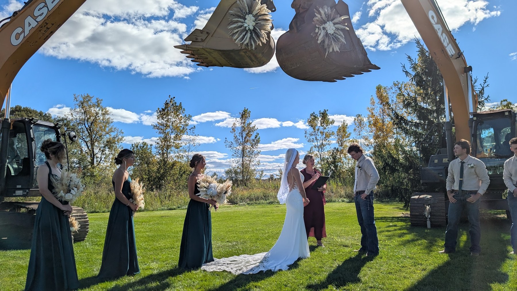 Tammy officiating an outdoor wedding beneath a unique floral arch made with excavators